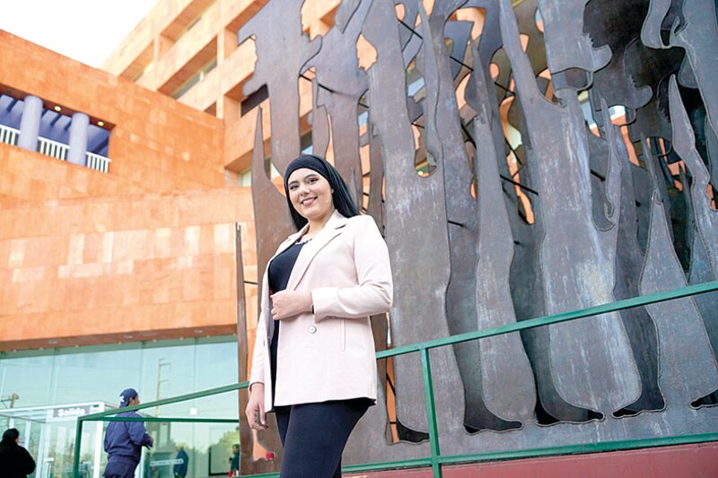 Estudiante universitaria posando junto a una escultura de metal.