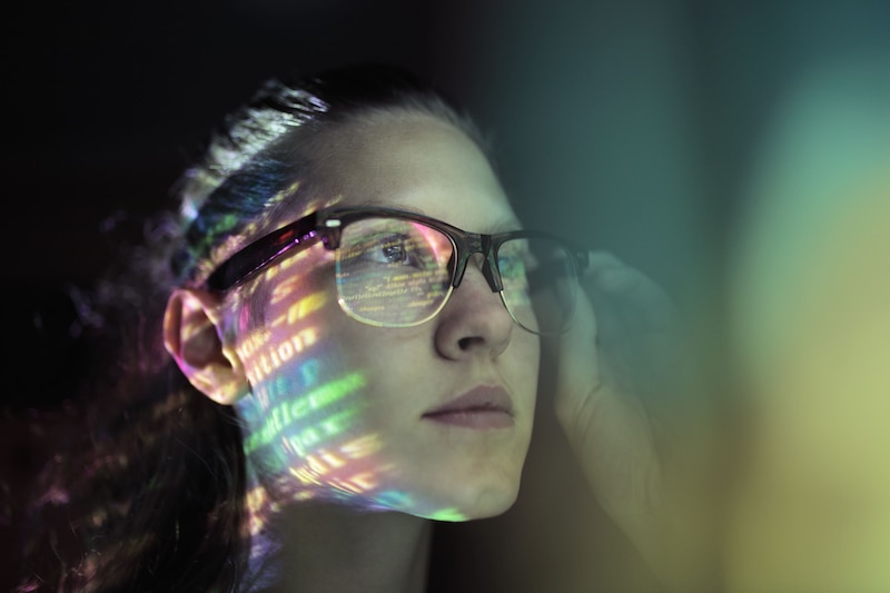 Mujer observando código reflejado en su rostro, representando el avance femenino en STEM