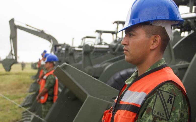 Soldado colombiano en uniforme y casco azul observa maquinaria pesada en una zona rural