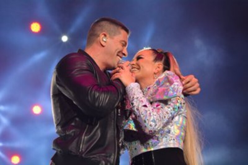 CNCO y Karol G cantando juntos en un concierto.