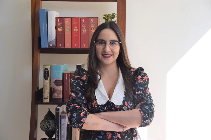 Mujer joven con gafas y un vestido negro con estampado de flores.