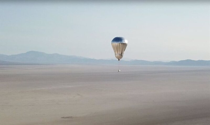 Un globo aerostático plateado vuela sobre un desierto.