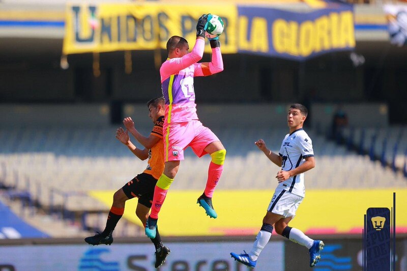 El portero de Pumas, Alfredo Talavera, detiene un balón con una mano.