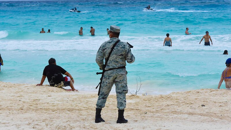 Un soldado vigila la playa mientras la gente nada y se relaja