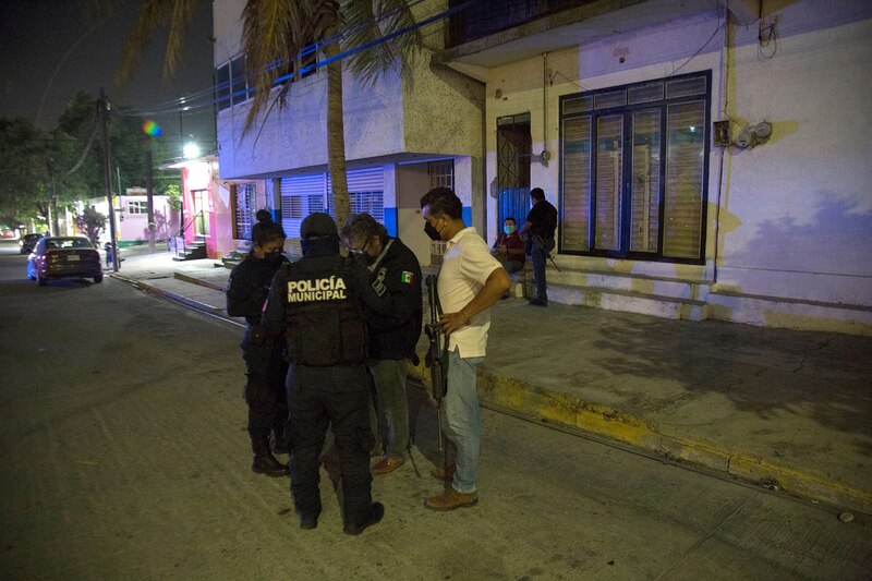 Policía detiene a un grupo de personas en una calle oscura.