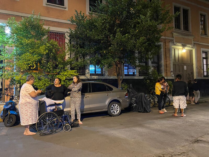 Un grupo de personas espera en la calle junto a un automóvil.