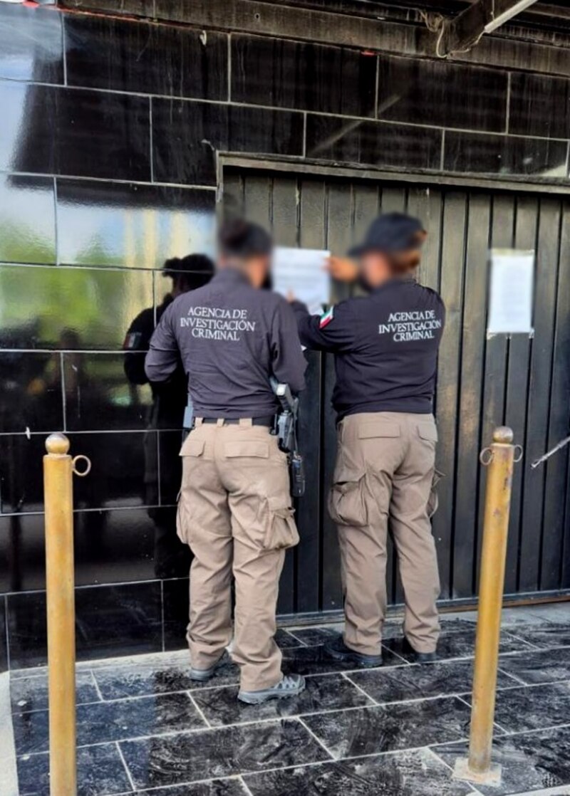 Dos agentes de la policía de investigación criminal están colocando un cartel en la puerta de un local.