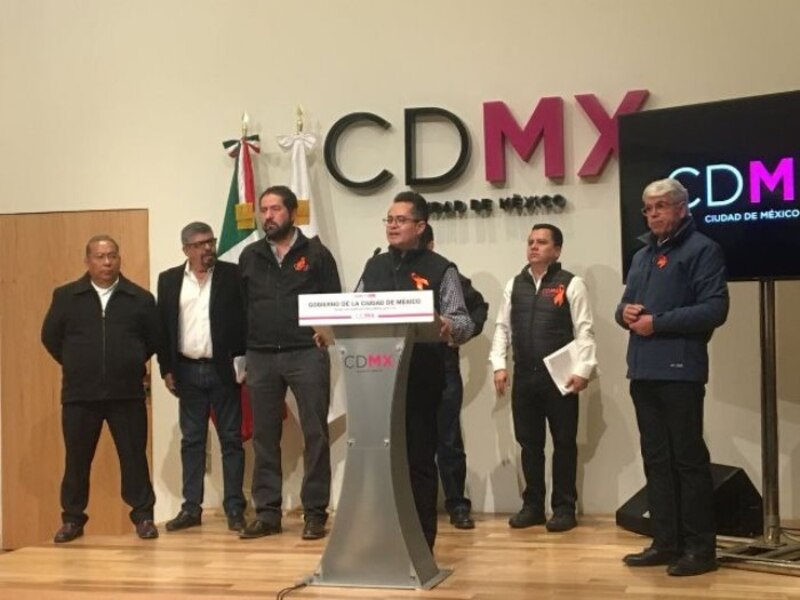 Un grupo de hombres en un podio con el logo de la Ciudad de México al fondo