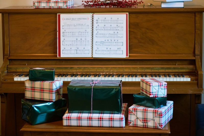 Imagen de regalos navideños frente a un piano para ejemplificar la música de las fiestas decembrinas.