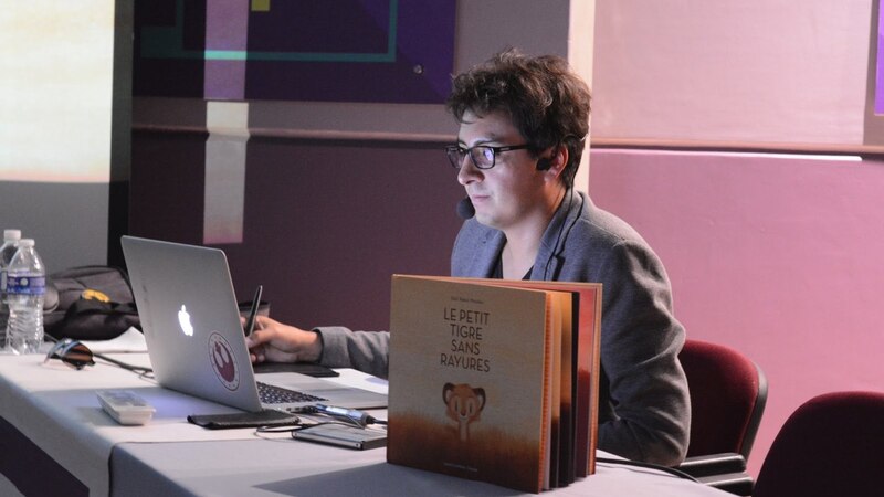 Un hombre sentado en una mesa con un ordenador portátil y un libro.