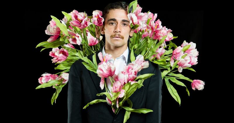 Un hombre con un traje negro y flores rosas
