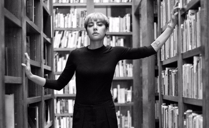 La imagen muestra a una mujer joven en una biblioteca.