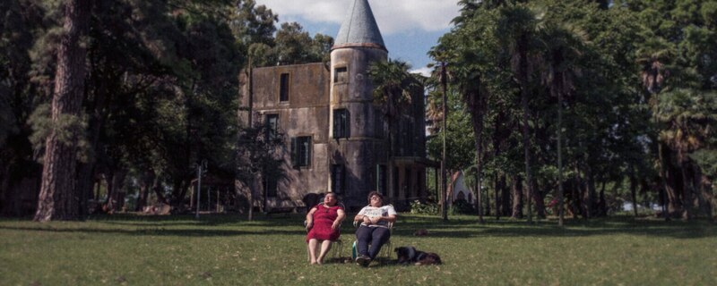 Dos mujeres sentadas en el jardín de una mansión.