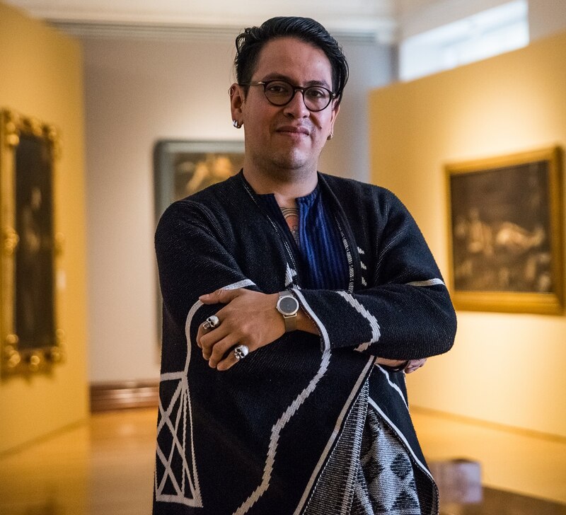 Un hombre joven con gafas y un suéter negro con un reloj inteligente en la muñeca se encuentra en un museo.