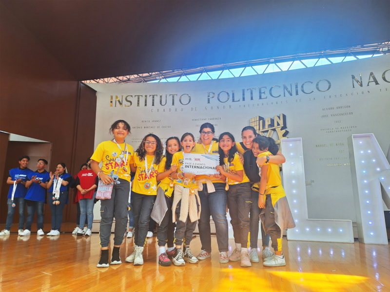 Un grupo de estudiantes de primaria con un cartel que dice "Pase a Evento Internacional".