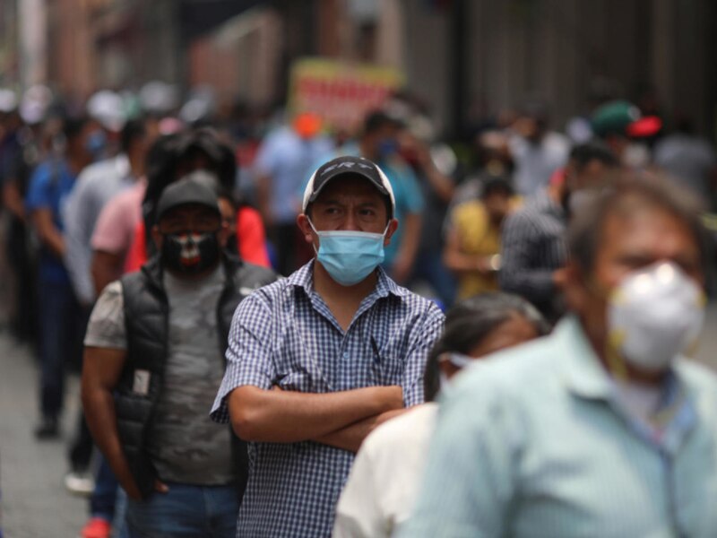 Un hombre con una mascarilla en la cara está de pie en una calle llena de gente