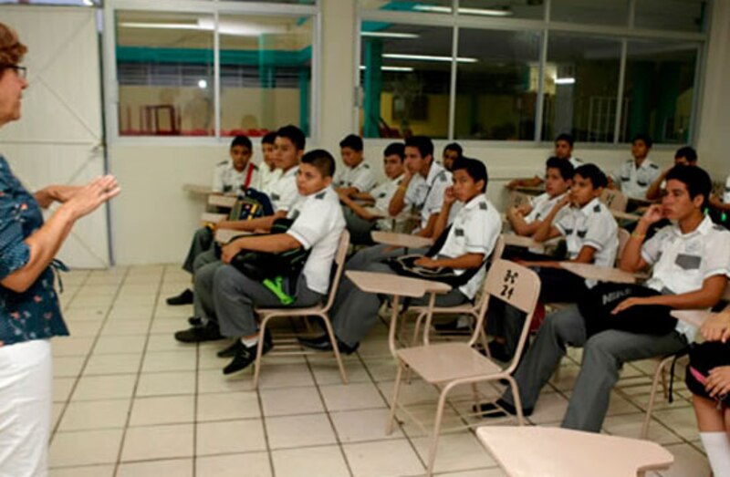 Profesora dando clase a un grupo de estudiantes en un aula.