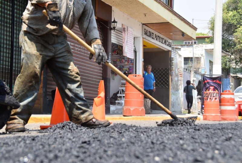 Trabajador de la construcción usando una escoba para esparcir asfalto caliente en una calle de la Ciudad de México.