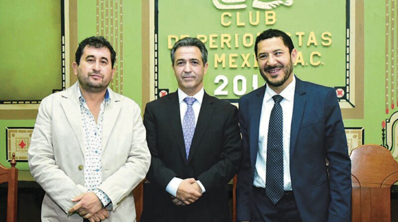 Tres hombres sonríen y se dan la mano en un evento del Club de Periodistas de México.