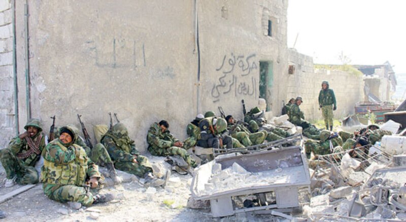 Combatientes sirios descansan en una calle destruida