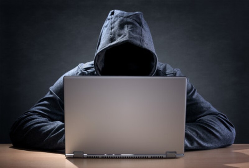 Ciberdelincuente encapuchado usando un ordenador portátil en la oscuridad
