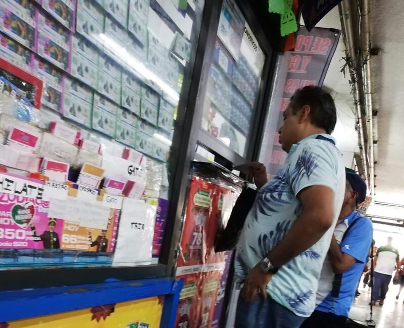 Personas eligiendo boletos de la Lotería del Zodiaco en un puesto de la estación Allende del Metro de la Ciudad de México, donde tradición y esperanza se entrelazan.