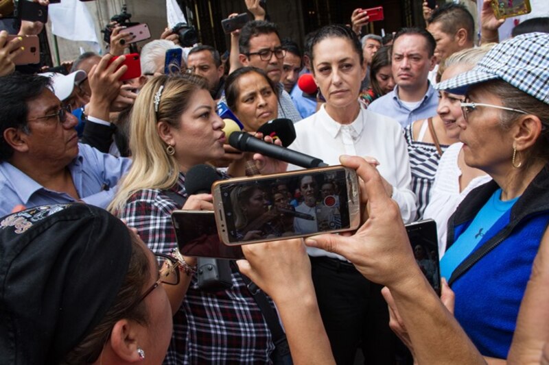 Periodista rodeada de personas que la entrevistan y graban con sus teléfonos móviles