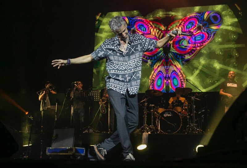 Un cantante actúa en un concierto con una mariposa gigante en la pantalla de fondo.