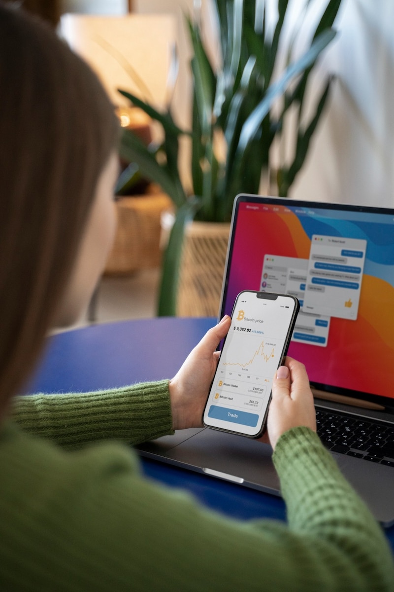 Persona usando una aplicación financiera en el celular frente a una laptop