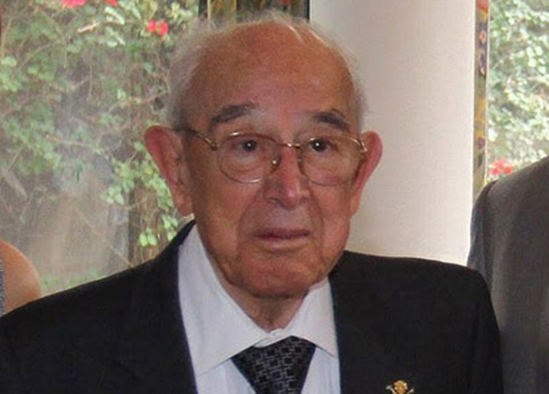 Un anciano con gafas y traje mira a la cámara.