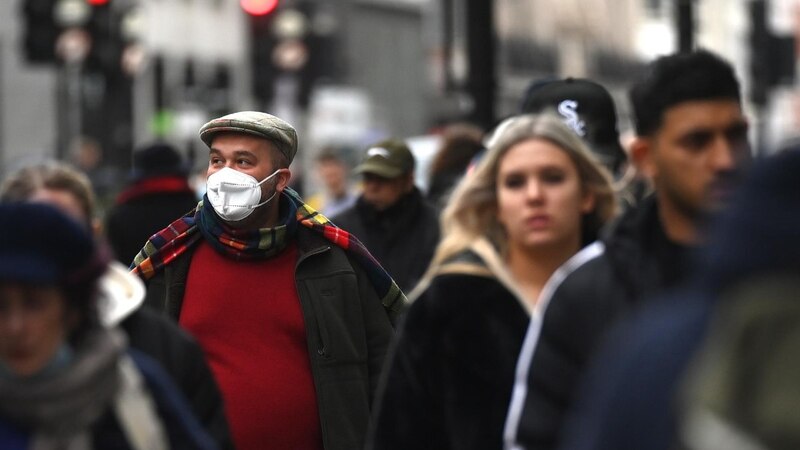 Un hombre con mascarilla camina por una calle concurrida