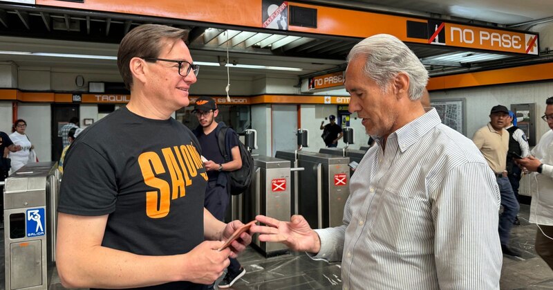 Dos hombres están usando sus teléfonos móviles en el metro de la Ciudad de México.