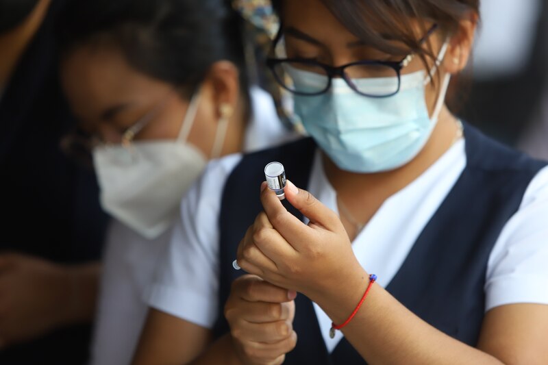 Mujer joven con mascarilla sosteniendo una jeringa con una vacuna.