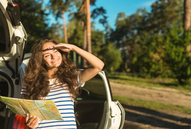 Mujer leyendo un mapa al lado de su coche