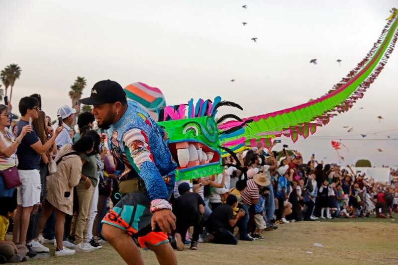 Un hombre sostiene una cometa en forma de dragón durante un festival.