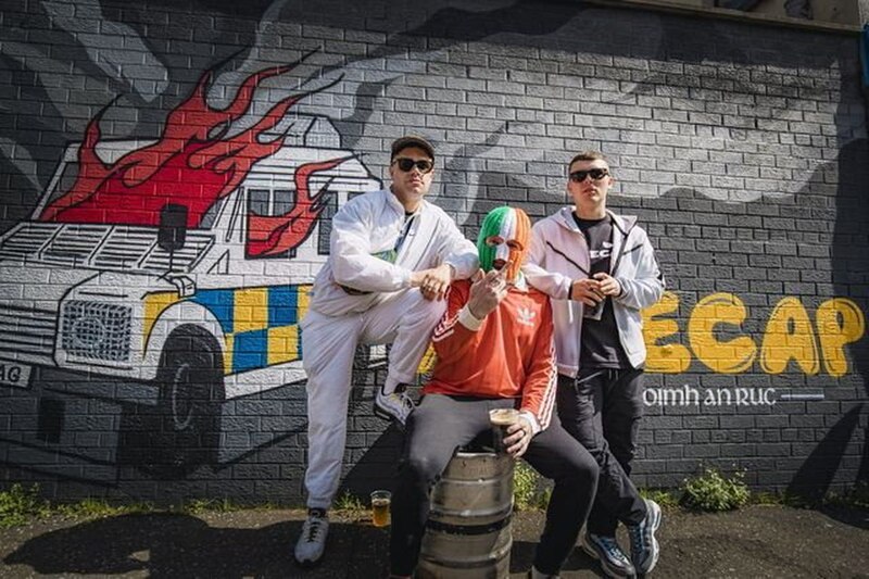 Tres hombres vestidos con ropa casual están posando frente a un mural en la calle.