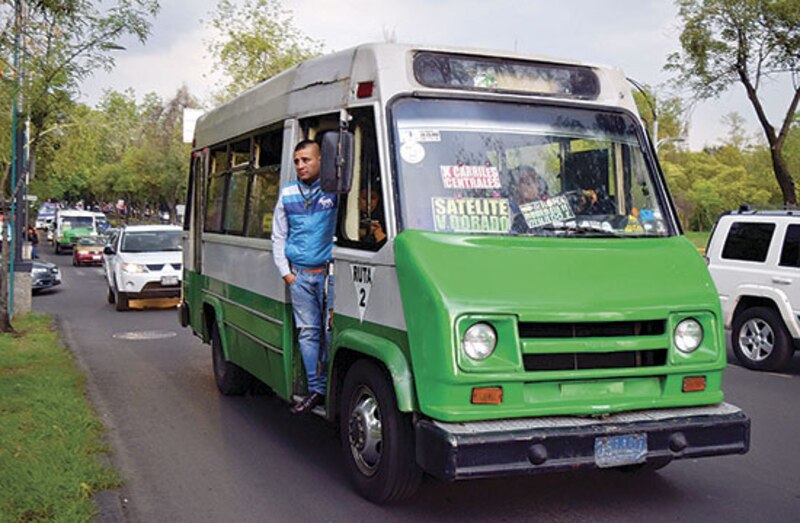 Un hombre viaja en la puerta de un autobús en la Ciudad de México.