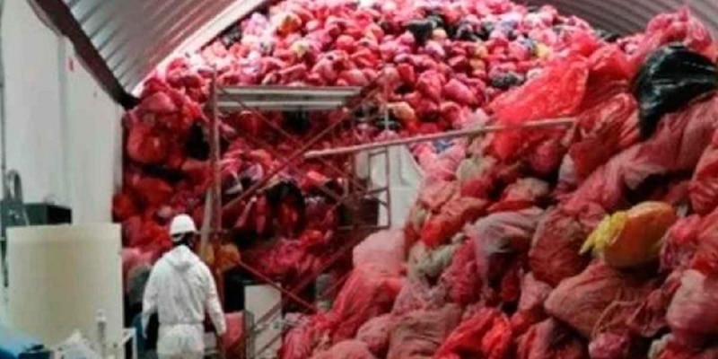 Un trabajador con traje de protección inspecciona una montaña de bolsas rojas de basura