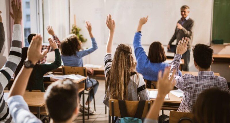 Estudiantes en el aula levantando la mano para responder