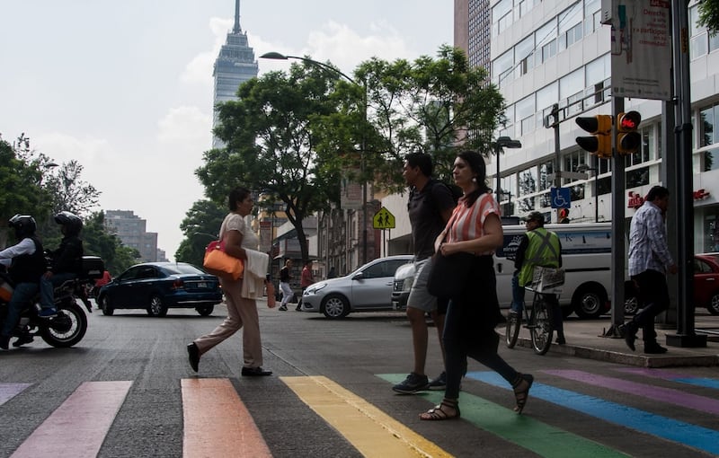 Peatones cruzan la calle en un paso de cebra pintado con los colores del arco iris.