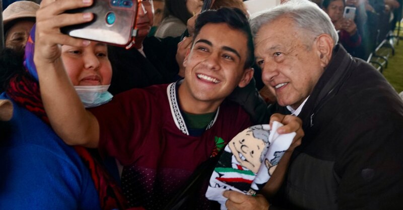 El presidente López Obrador se toma una selfie con un joven durante un evento público.