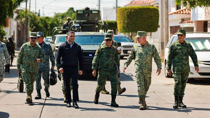 El presidente López Obrador camina junto a militares en una calle de México.