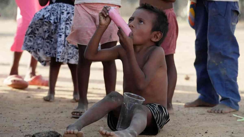 Niño indígena bebe de una bolsa plástica