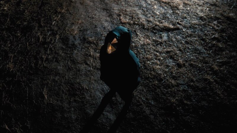 La imagen muestra a una persona encapuchada caminando en la oscuridad.