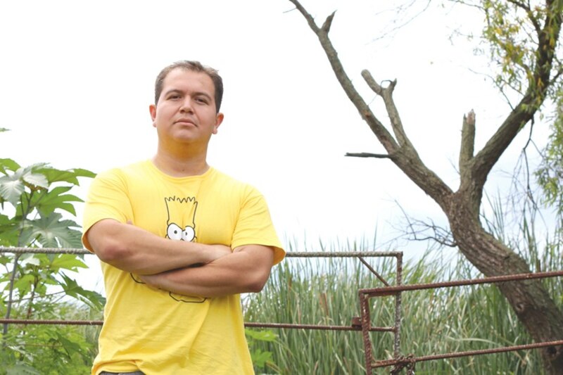 Un hombre con una camiseta amarilla de Los Simpsons se encuentra en un campo mirando a la cámara con los brazos cruzados.