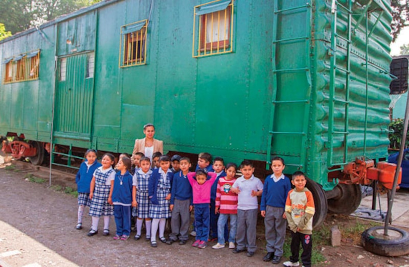 Niños y niñas sonríen frente a un vagón de tren verde