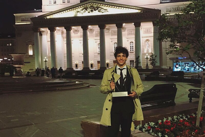 Un joven músico recibe un premio frente a un teatro.