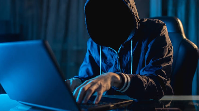 Ciberdelincuente encapuchado usando una computadora portátil en la oscuridad