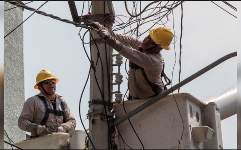 Dos trabajadores de la compañía eléctrica arreglando un cable en lo alto de un poste