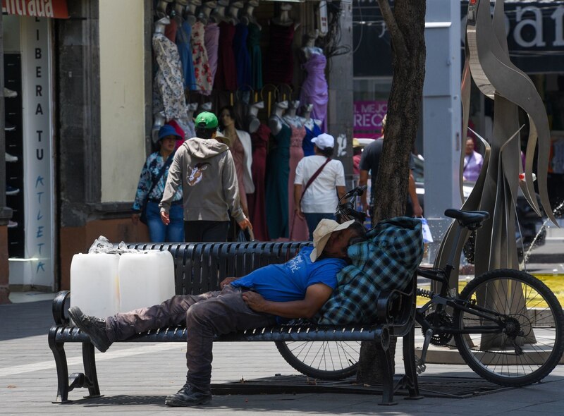 Un hombre sin hogar duerme en una banca en la Ciudad de México